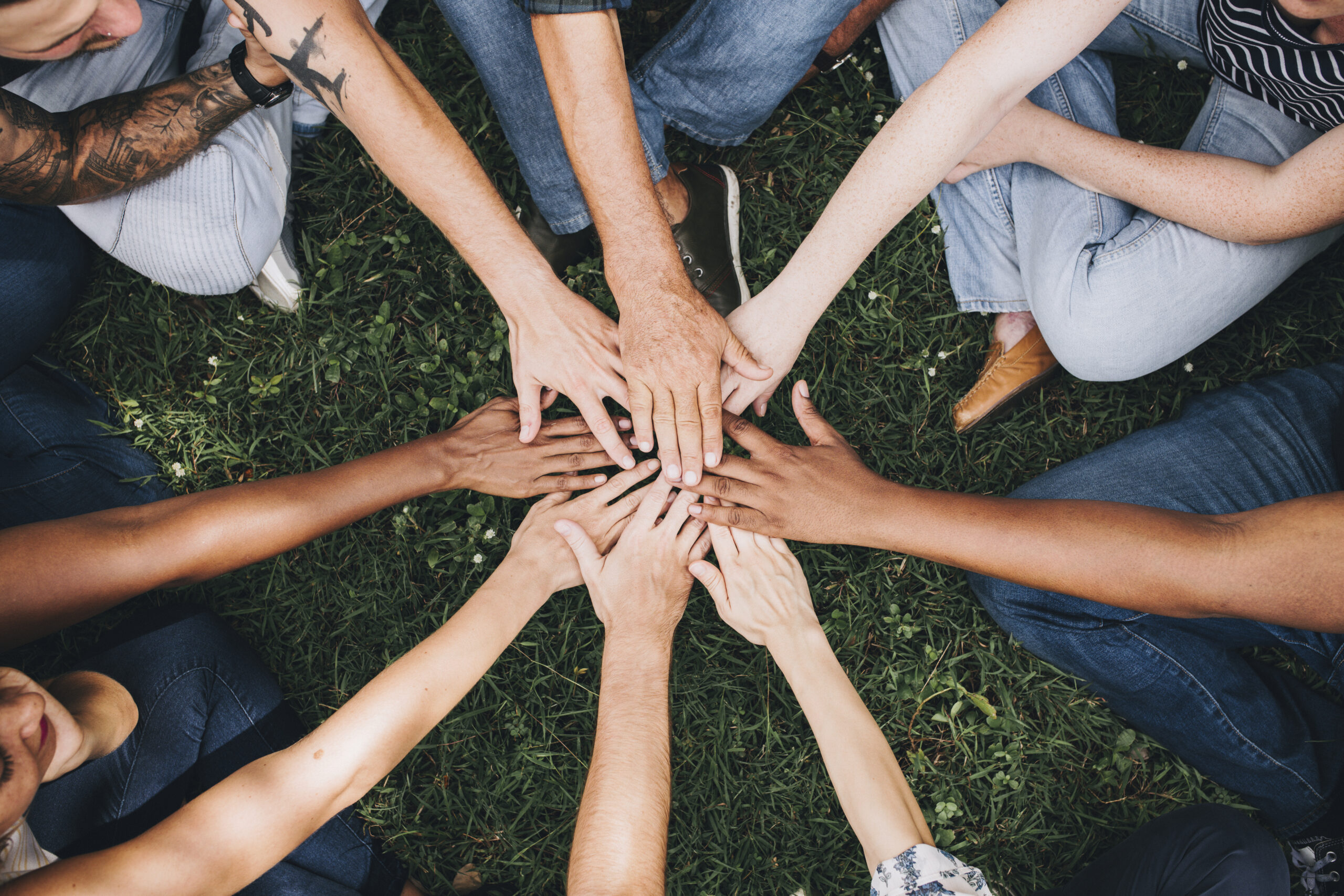 People stacking hands together in the park Symbolbild Zusammenhalt in der Pflege - Acht Hände die im Kreis aufeinander liegen